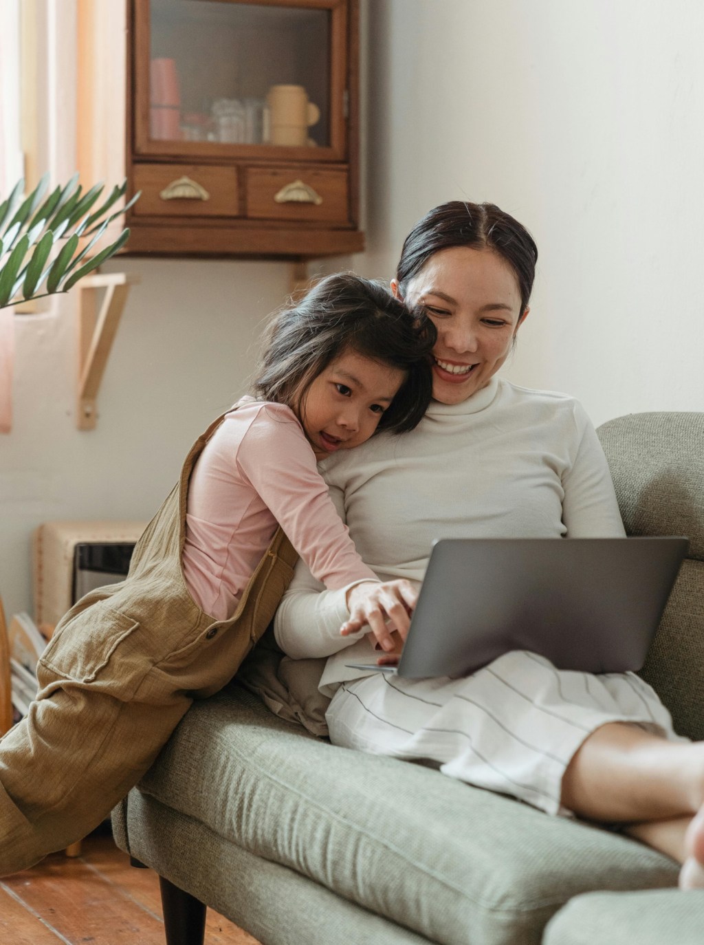 Asian mother works on laptop at home with daughter